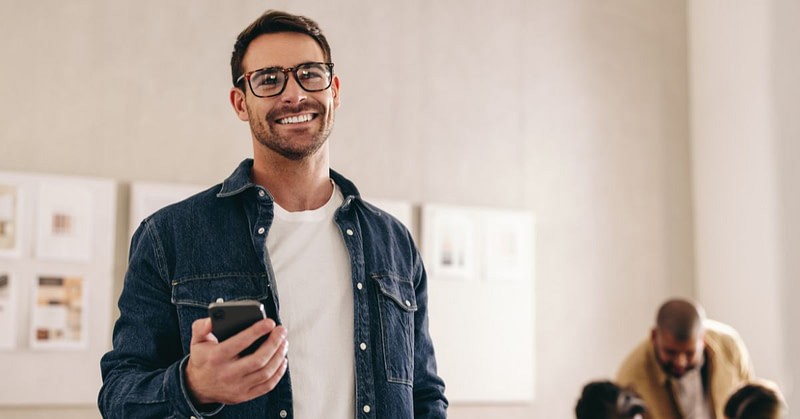 Mies seisoo puhelin kädessään, hän on juuri varannut itselleen lisää työvuoroja puhelimellaan.